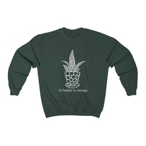 May include: A dark green sweatshirt featuring a white illustration of a potted plant and the text "it's better in vintage".