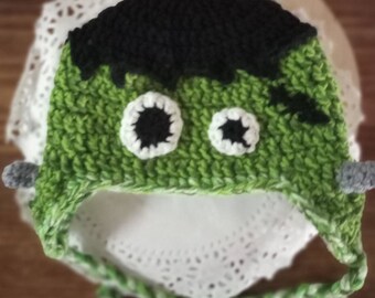 May include: Green and black crocheted hat with white eyes and a stitched-on scar. The hat has a long tie that can be tied under the chin.
