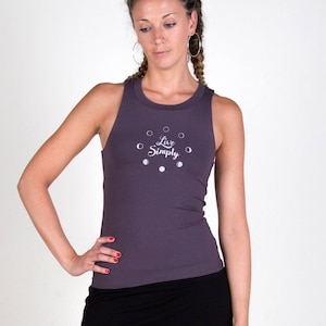 以下が含まれることがあります： 「Live Simply」という文字が書かれたグレーのタンクトップと黒いスカートを着用した女性。タンクトップには白いドットのある円形のデザインが施されています。