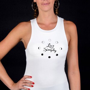 以下が含まれることがあります： 三日月と「Live Simply」というテキストの黒いグラフィックが描かれた白いタンクトップです。