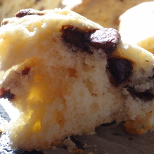 May include: A close-up of a freshly baked scone with chocolate chips. The scone is light and fluffy, with a slightly golden brown crust. The chocolate chips are melted and gooey, adding a sweet and decadent touch.