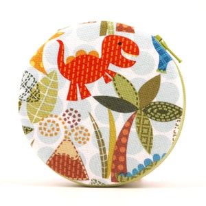 May include: A round, zippered pouch with a dinosaur theme. The pouch features a light blue background with a repeating pattern of white circles. A red dinosaur is the central image, surrounded by green and orange foliage. The zipper is green.