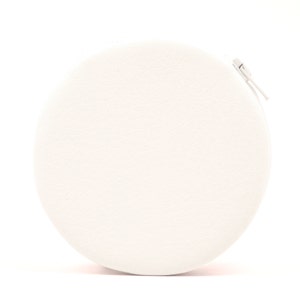 May include: A circular, cream-coloured pouch with a zip closure. The pouch has a textured finish and a small, white zip pull. The design is simple and minimalist, with a focus on the clean lines and neutral colour.