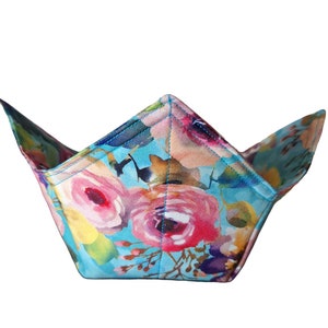 Może przedstawiać: Ocieplacz do misek z niebieskiego i różowego materiału w kwiatowy wzór. Ocieplacz wykonany jest z bawełny i ma za zadanie utrzymywać miski w cieple lub chłód.