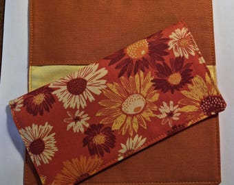 May include: An orange fabric checkbook cover with a matching wallet. The wallet features a floral pattern with orange, yellow, and white flowers. The checkbook cover is a solid orange color with a yellow accent.