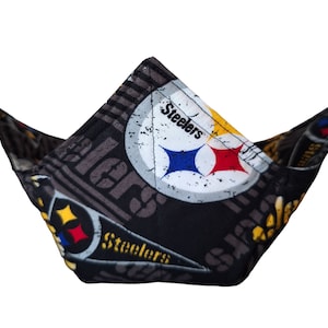 May include: A black fabric bowl with a Pittsburgh Steelers logo and the word "Steelers" repeated on the fabric. The bowl is folded in half and is sitting on a white background.