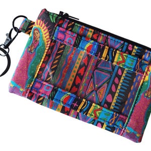 May include: A colourful zippered pouch with a clear window, featuring a repeating pattern of stripes, hearts, and geometric shapes. The pouch has a black metal key ring attached and a colourful image of a religious figure.