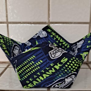 Op de afbeelding: Een blauwe en groene stoffen kom met het logo van de Seattle Seahawks en de woorden "Seattle Seahawks".