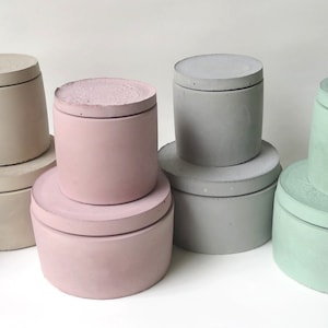 Puede incluir: Conjunto de seis contenedores de almacenamiento de hormigón con tapas. Los contenedores son de varios colores, incluyendo azul claro, rosa, beige y verde.