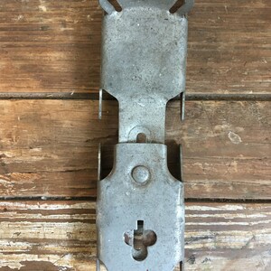 May include: A silver metal bracket with two holes at the top and a keyhole at the bottom. The bracket is designed to be mounted to a wall or other surface.