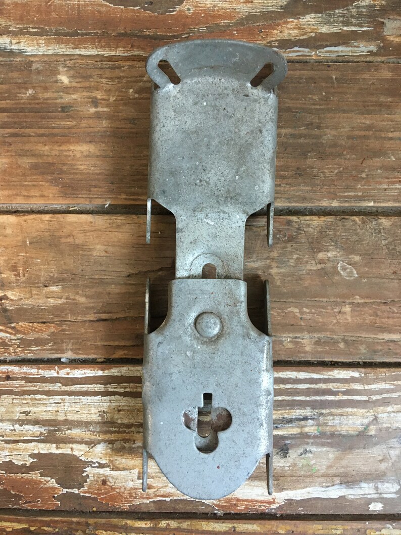 May include: A silver metal bracket with two holes at the top and a keyhole at the bottom. The bracket is designed to be mounted to a wall or other surface.