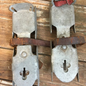 May include: A pair of vintage metal ice skate attachments with leather straps and red rubber pads. The metal is silver and shows signs of wear.
