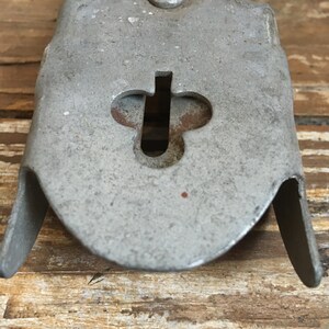 May include: Close-up of a silver metal object with a keyhole shaped like a clover. The object has a rounded shape and a smooth surface.