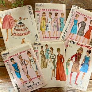 May include: A collection of vintage sewing patterns for women's clothing. The patterns are from McCall's and Simplicity and feature a variety of styles, including dresses, skirts, and jumpsuits. The patterns are in various colors, including blue, red, green, and white.