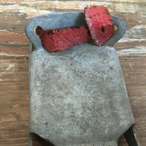 May include: A vintage metal bell with a red leather strap. The bell is weathered and shows signs of age.