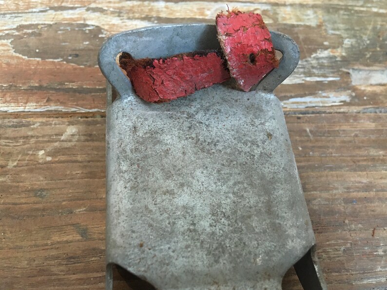 May include: A vintage metal bell with a red leather strap. The bell is weathered and shows signs of age.