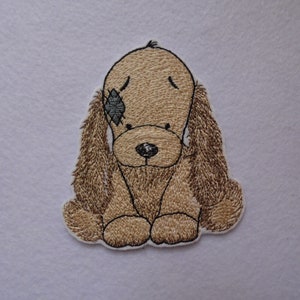 May include: Embroidered patch of a brown and white dog with a black eye patch. The dog is sitting with its head down and its ears flopped over.