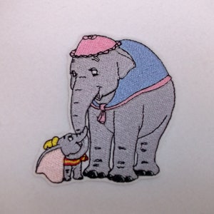 May include: Embroidered iron-on patch featuring a grey elephant with a pink hat and a blue cape, standing next to a smaller grey elephant with a pink cape and yellow ears.
