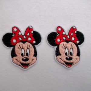 May include: Two embroidered iron-on patches featuring a cartoon image of Minnie Mouse with a red bow with white polka dots.