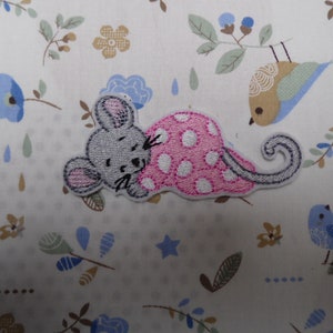 May include: An iron-on patch featuring an embroidered grey mouse wearing a pink polka dot blanket, asleep.