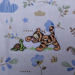 May include: Embroidered patch featuring a cartoon tiger with a pink nose, walking towards a green turtle. The patch is on a white background with a floral pattern.