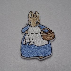 May include: Iron-on patch featuring Peter Rabbit in a blue dress holding a basket.