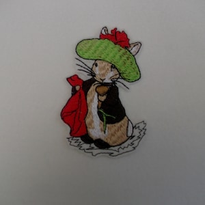 May include: Embroidered patch of a brown rabbit wearing a green hat with a red flower, holding a red flower and a green stem. The rabbit is wearing a black jacket and has white fur on its chest.