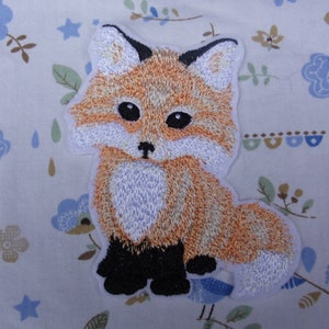 May include: Embroidered iron-on patch of a cute orange fox with black eyes and black feet. The fox is sitting with its tail curled behind it.