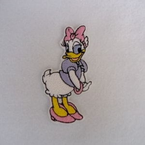 May include: An embroidered iron-on patch featuring a cartoon image of a duck with a pink bow, purple dress, and yellow shoes.