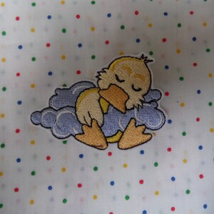 May include: An embroidered patch featuring a sleeping duck on a blue cloud. The duck has its eyes closed and its wings are folded. The cloud is outlined in white.