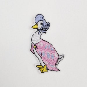 May include: Embroidered patch of a white goose wearing a pink dress and a blue bonnet. The goose is standing on one leg and looking to the left.