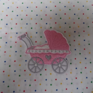 May include: Pink and grey embroidered baby carriage applique patch. The carriage has a white trim and a small heart on the front.