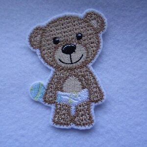 May include: Embroidered brown teddy bear applique with a blue and yellow ball in its hand. The bear is wearing a white nappy.
