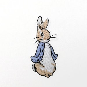 May include: Embroidered patch featuring a rabbit in a blue jacket. The rabbit has tan and white fur, with black whiskers and a detailed facial expression. The patch is designed for application on clothing or accessories.