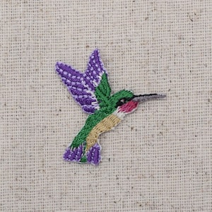 Puede incluir: Aplique de colibrí bordado en morado, verde y rojo.