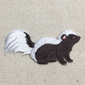 Könnte beinhalten: Gestickter Bügelaufkleber mit einer schwarz-weißen Stinktier mit rosa Nase. Das Stinktier schaut nach rechts und hat einen weißen Schwanz mit einem schwarzen Streifen.