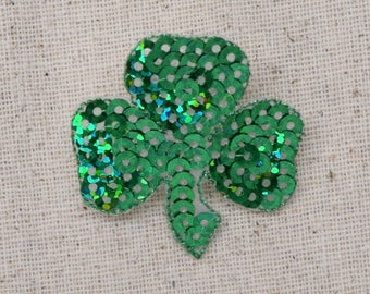 May include: A green shamrock made of iridescent sequins. The shamrock is a traditional Irish symbol of good luck.