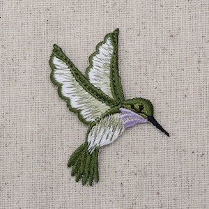 Puede incluir: Parche de aplique de colibrí bordado en verde y blanco. El colibrí está en vuelo con las alas extendidas.