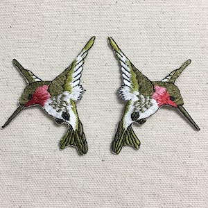 Puede incluir: Dos parches bordados de colibrí verde y blanco con picos rojos y acentos rojos en el pecho.