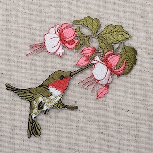 Puede incluir: Parche bordado con un colibrí verde con el pecho rojo, posado en una rama de flores rosas y blancas con hojas verdes.