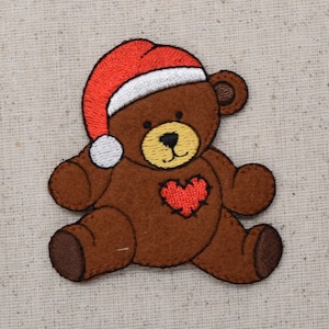 May include: Brown felt teddy bear wearing a red Santa hat with a white trim. The bear has a red heart sewn on its chest.