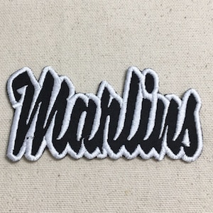 Pode incluir: Etiqueta bordada preta e branca com a palavra "Marlins" em uma fonte estilizada.