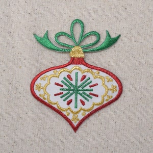 May include: Embroidered Christmas ornament patch in red, white, green, and gold. The ornament has a teardrop shape with a green bow at the top. The design features a snowflake and floral pattern.