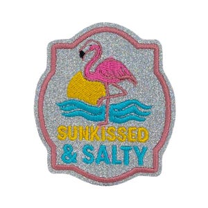 May include: Embroidered patch featuring a pink flamingo, yellow sun, and blue waves. The text "Sunkissed & Salty" is in yellow and blue. The patch has a silver glitter background and a pink border.