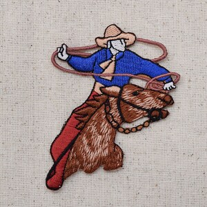 Puede incluir: Parche bordado de un vaquero montando un caballo marrón, con una camisa azul, pantalones rojos y un sombrero marrón. El vaquero sostiene un lazo en su mano derecha.