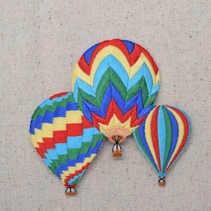 May include: Three embroidered hot air balloons in red, yellow, blue, and green. The balloons are arranged in a cluster with the largest balloon in the center.
