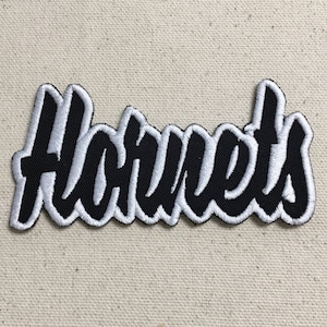May include: A black and white embroidered patch with the word "Hornets" in a stylised font.