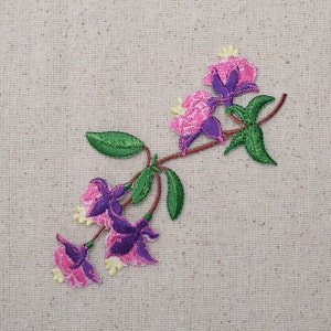 May include: Embroidered patch featuring a pink and purple flower sprig with green leaves. The flowers have a delicate, feminine design.