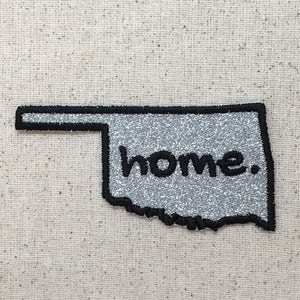 May include: A silver glitter outline of the state of Oklahoma with the word "home." embroidered in black.