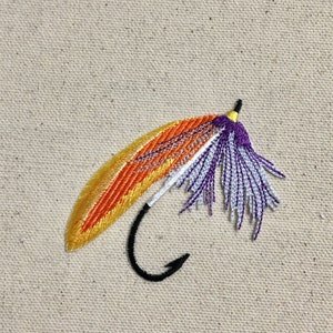 Könnte beinhalten: Ein lila und orangefarbener Fliegenfischköder mit einem schwarzen Haken.